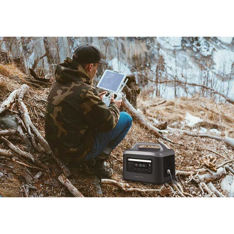 Person in camouflage jacket using a tablet in a forest setting with an Aeon Guardians G1200 portable power station nearby.