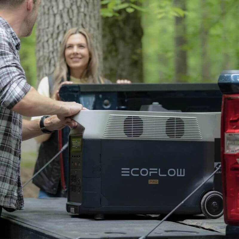 Two people using an EcoFlow Delta Pro power station device on a truck bed in a forest setting