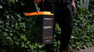 iTechworld iTECH100SX Slim Deep Cycle Lithium Battery with Bluetooth LiFePO4 100Ah - held by a person with a garden behind.